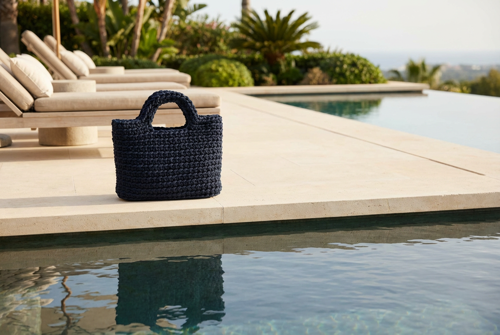 Navy woven handbag on a sun lounger by a poolside with palm trees in the background