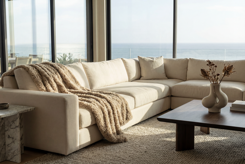 Beige sectional sofa in a living room with large windows and a view of the ocean.
