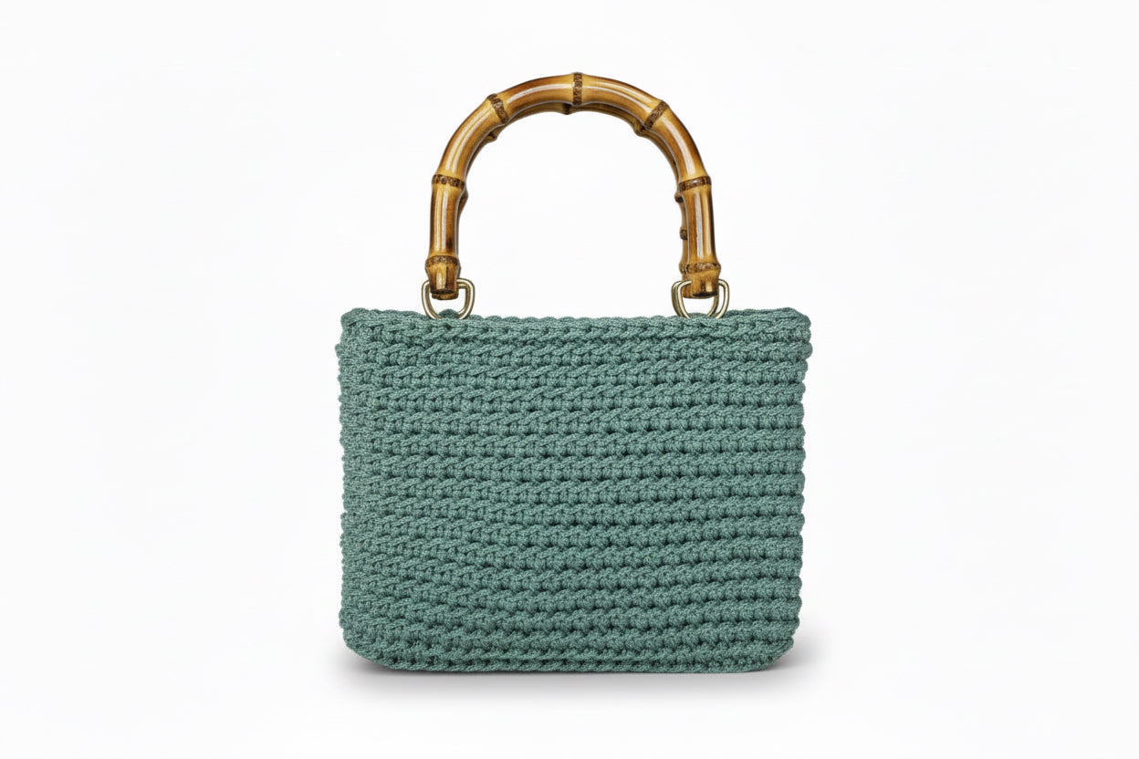 Sage green woven handbag with a bamboo handle on a white background